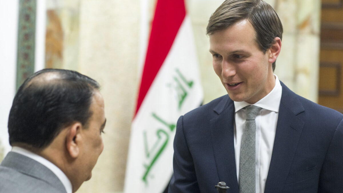 Jared Kushner speaks to someone with the Iraqi flag in the background