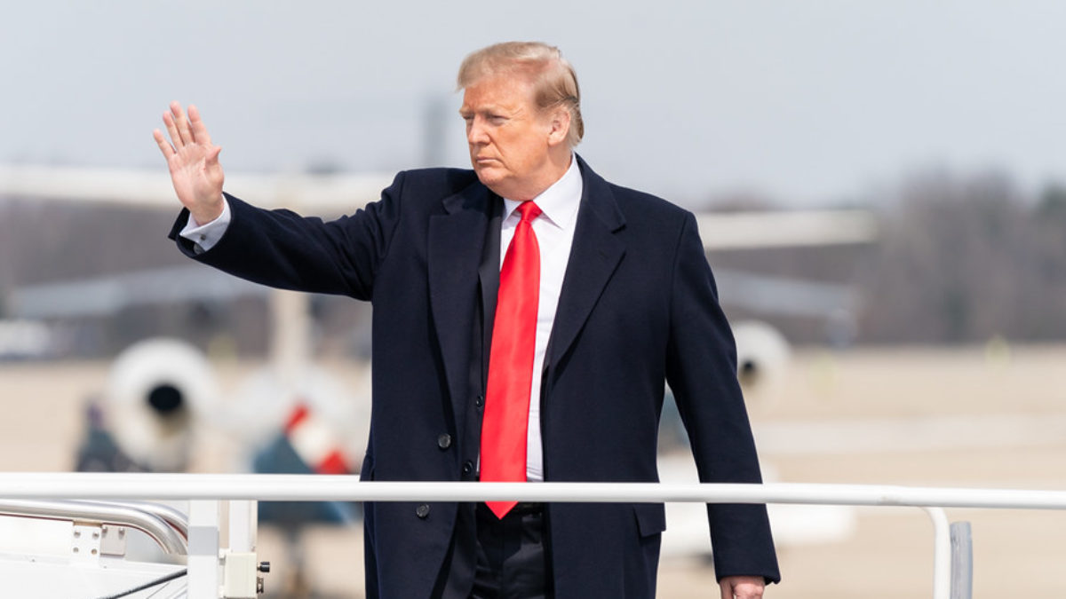 A stern-faced Donald Trump waves while boarding an airplane