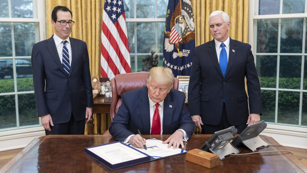 Steve Mnuchin and Mike Pence look on as Donald Trump signs a document in the Oval Office