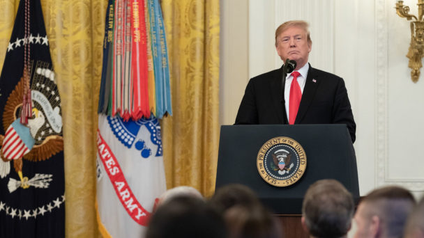 Donald Trump, looking stern, stands at a podium during an event