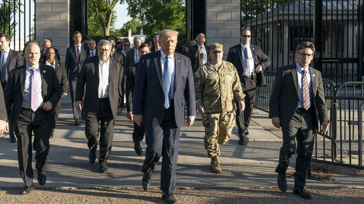 Donald Trump walks with Bill Barr and members of the military out of a gated area