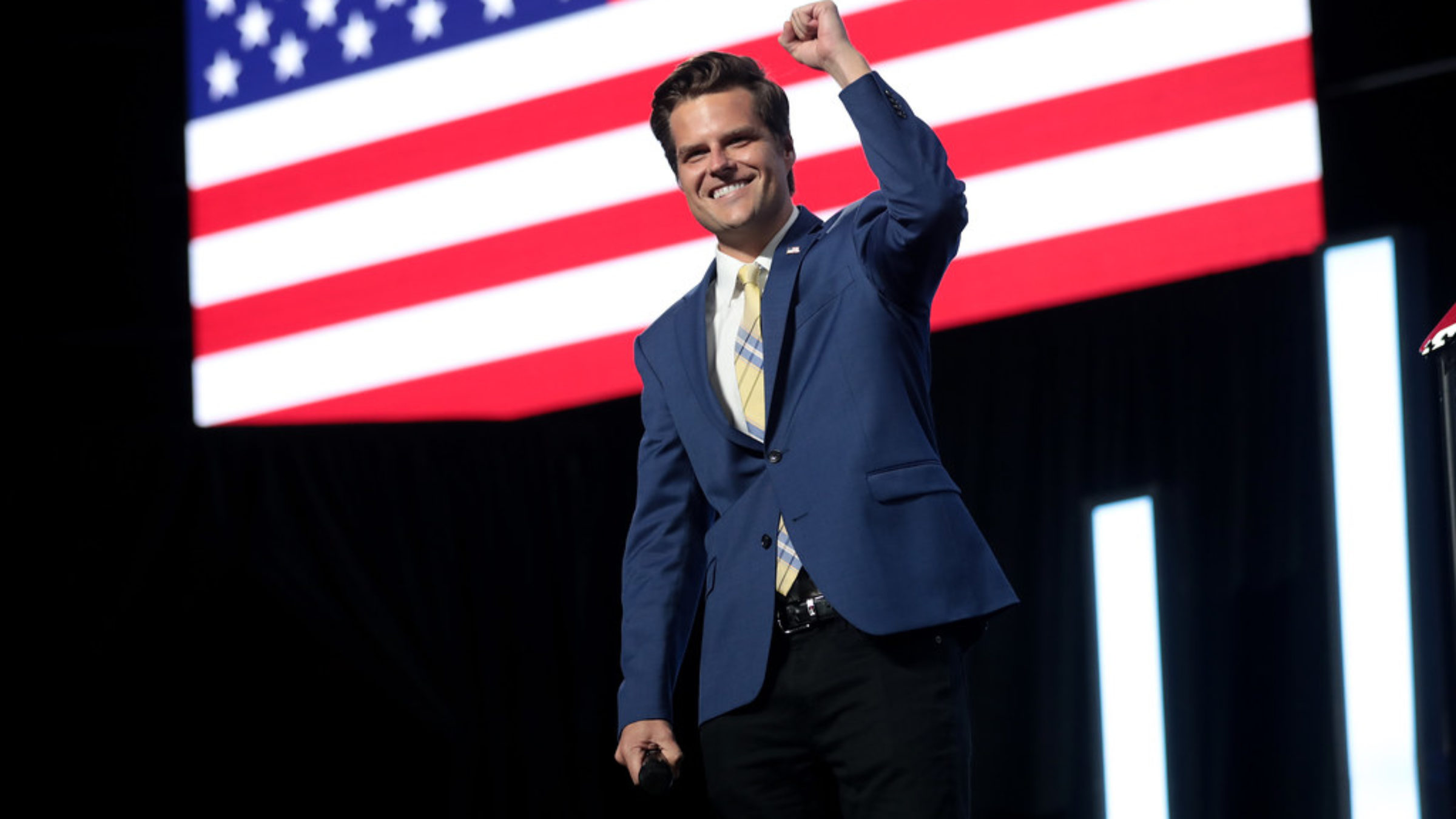 Matt Gaetz raises his fist against a backdrop of the American flag