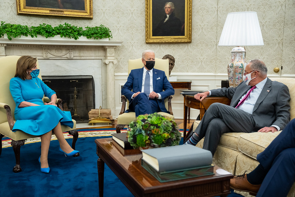 Nancy Pelosi and Chuck Schumer talking with President Joe Biden, all wearing masks.