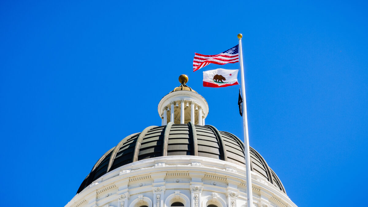 The US and the California state flag waving in the wind in front of the dome of the California State Capitol
