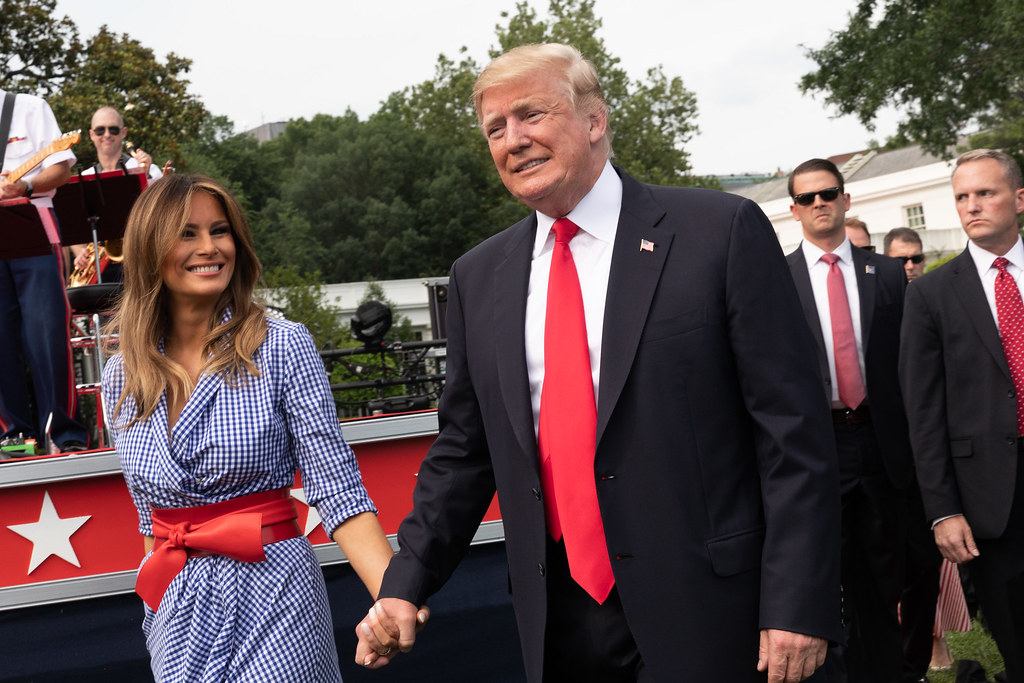 Donald Trump and Melania Trump smile and hold hands while walking through a Fourth of July event