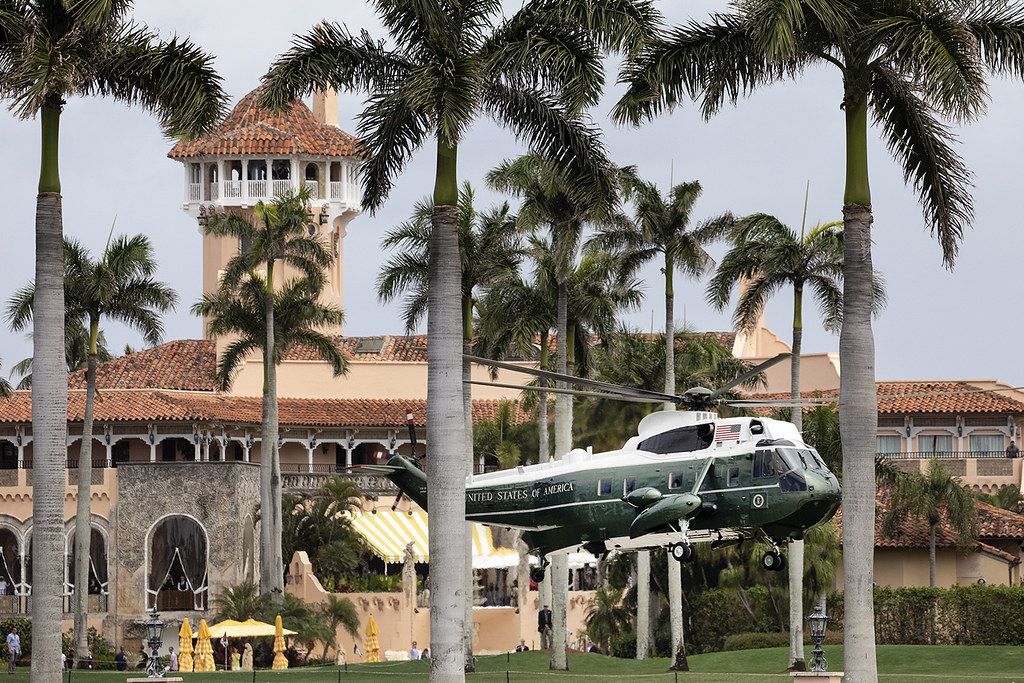 Marine One lands amongst a patch of palm trees at Mar-a-Lago