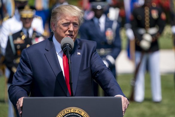 Trump speaks at a podium with several armed forces members in dress uniform in the background