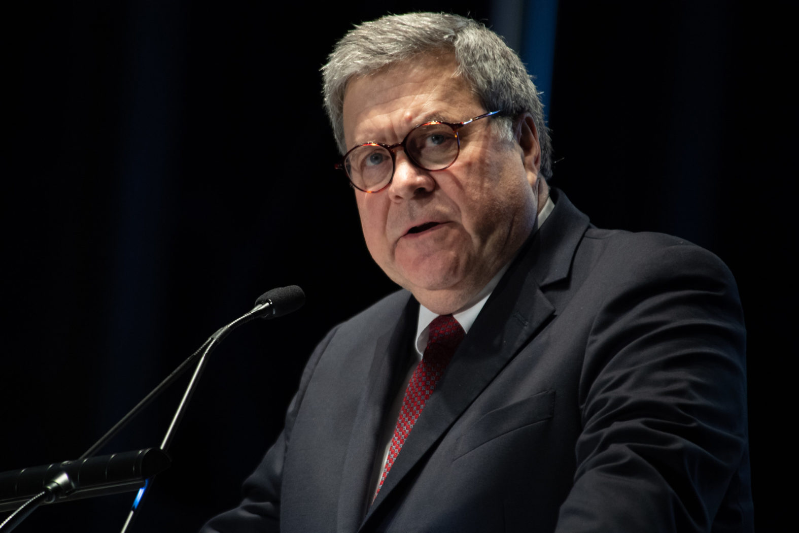 A stern Bill Barr speaks into a small microphone