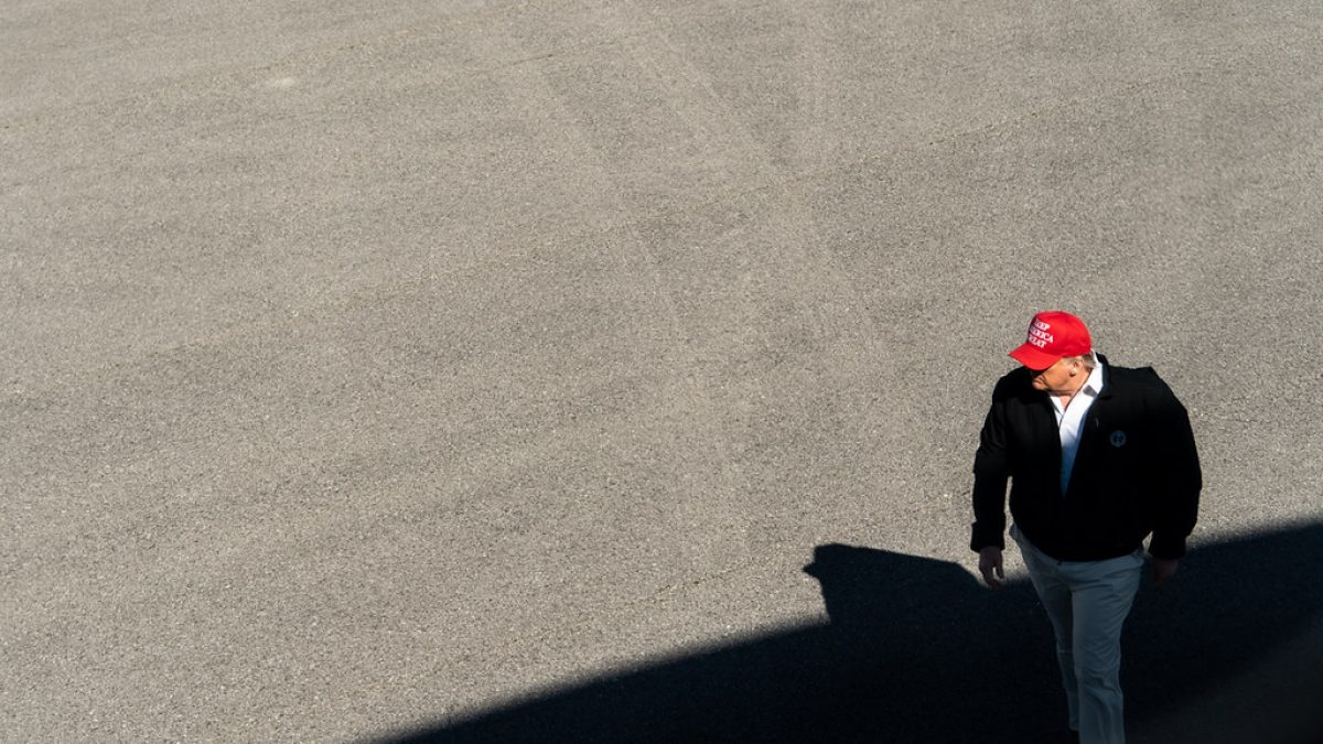 Donald Trump walks across a swath of pavement wearing a red "Make America Great Again" hat