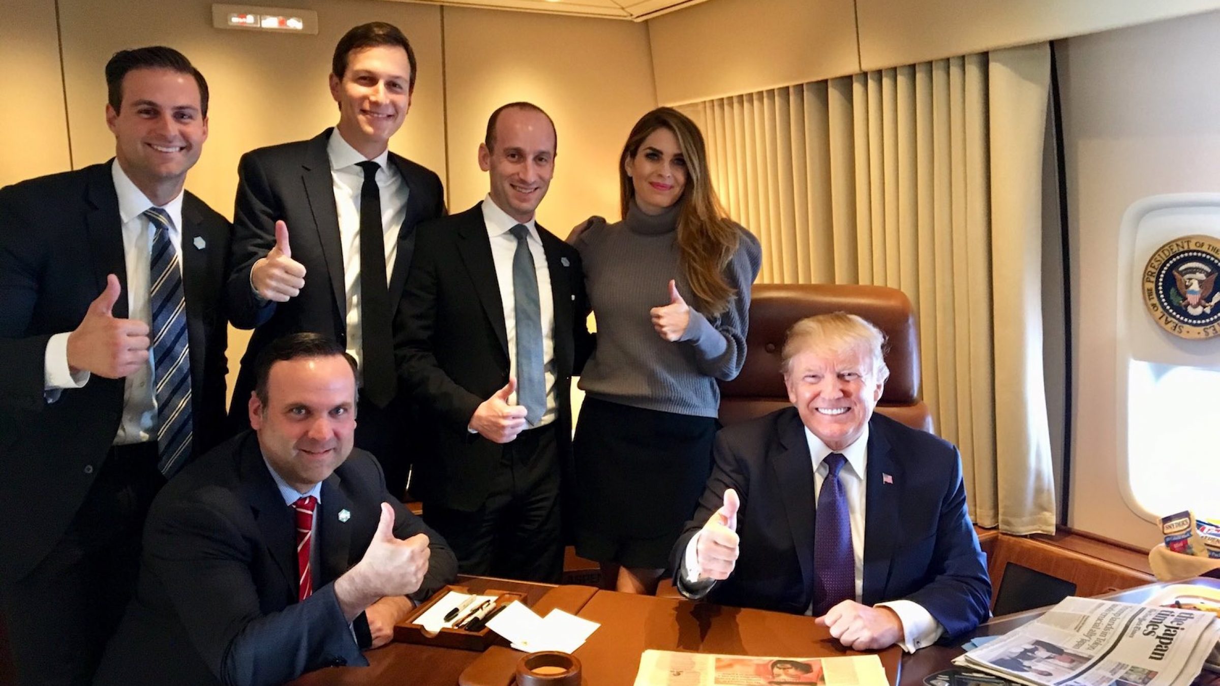 Donald Trump and several aides, including Hope Hicks and Jared Kushner, smile and give "thumbs up" signs while in the Air Force One office